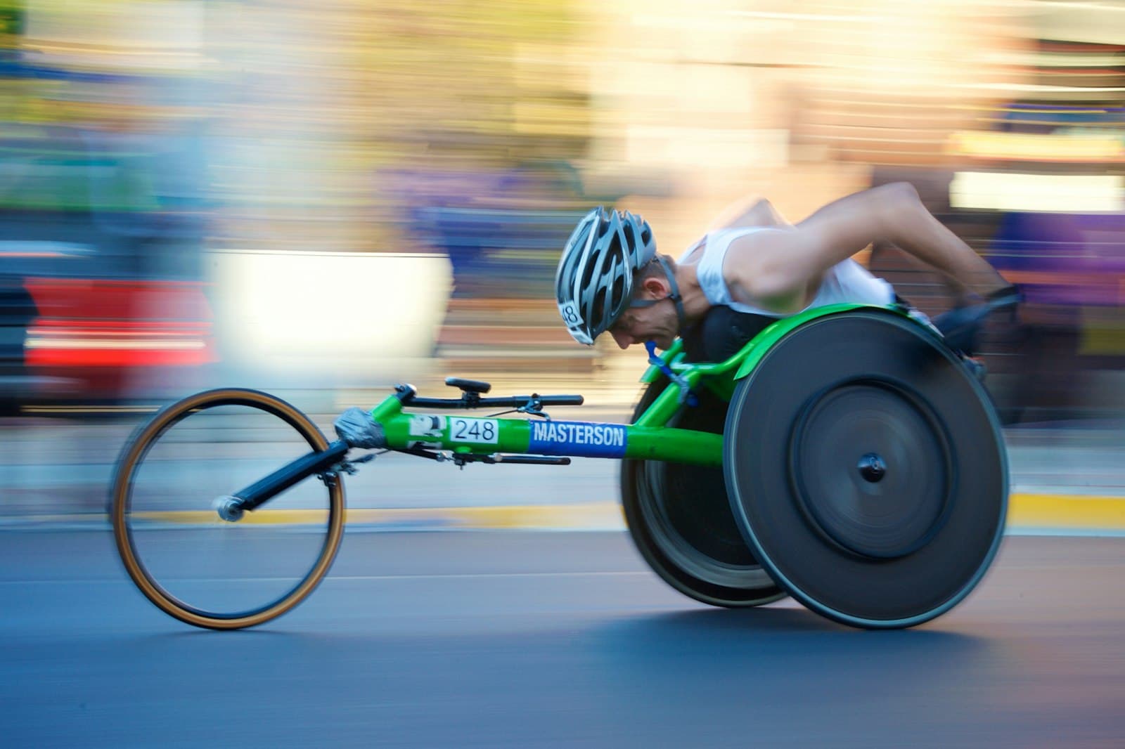 A wheelchair racer in full motion on a track, leaning low into the drive, the background blurred with speed.