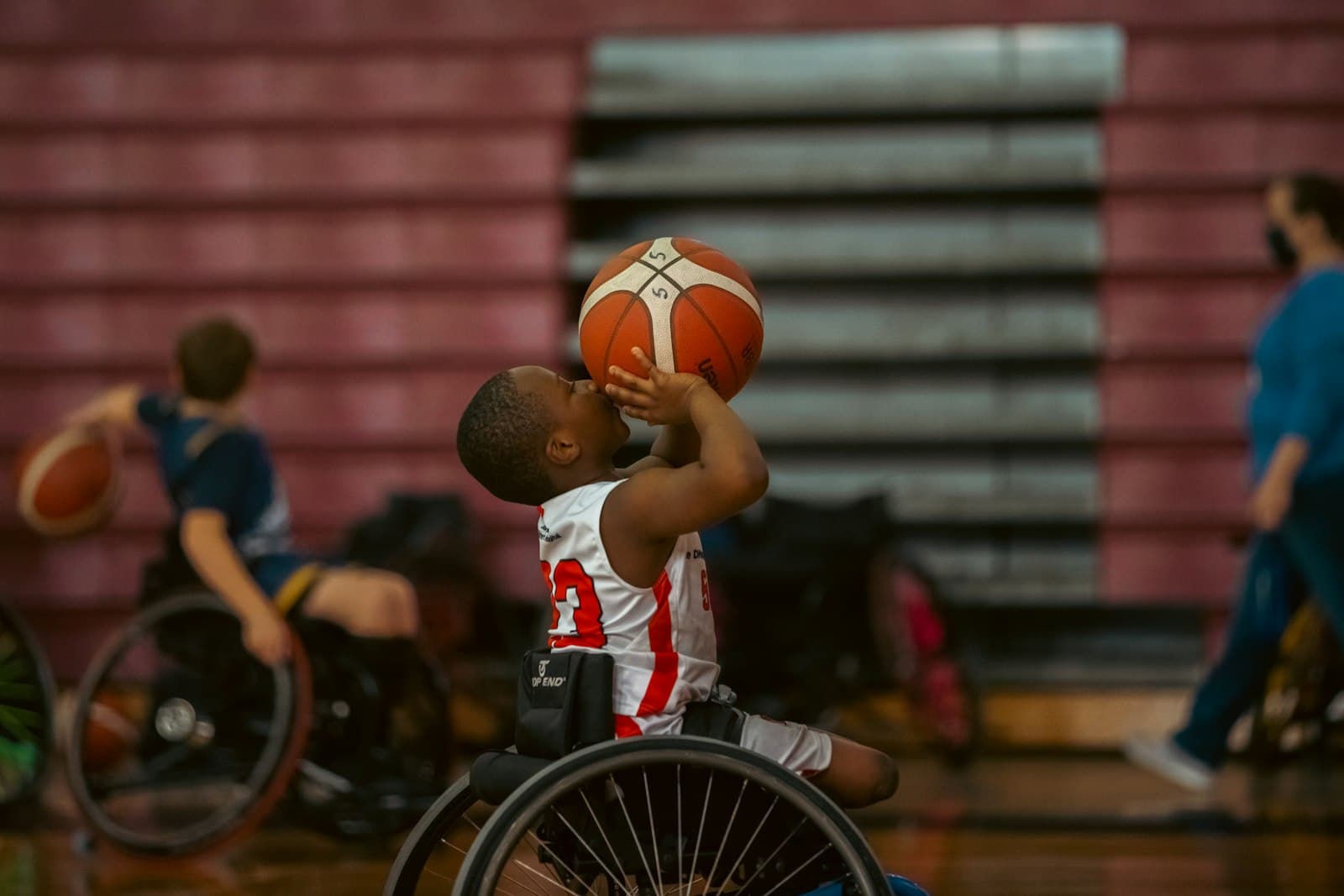 A wheelchair basketball player mid-game, reaching for the ball with intense focus.